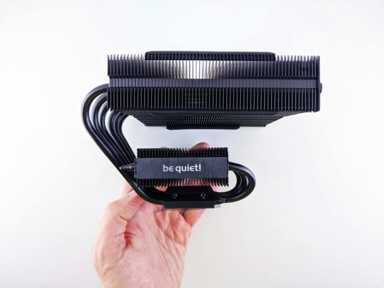 Close-up of a CPU cooler with a 'be quiet!' logo held in hand against a white background.